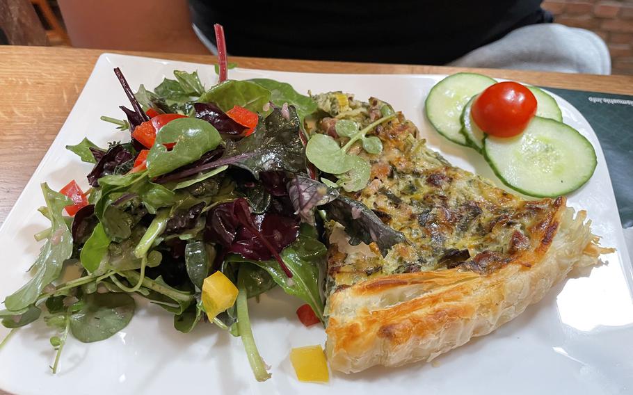 A golden brown quiche with a side of greens on a white plate.