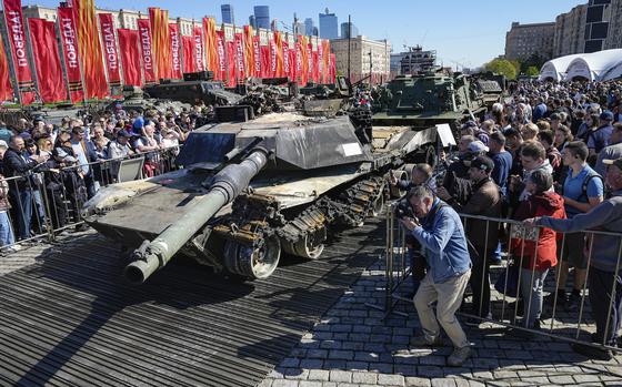 Visitors look at and take photos of a U.S. made M1A1 Abrams tank, foreground, hit and captured by Russian troops during the fighting in Ukraine which is seen on display in Moscow, on Wednesday, May 1, 2024. An exhibition of military equipment captured from Kyiv forces during the fighting in Ukraine has opened in the Russian capital. (AP Photo/Alexander Zemlianichenko)