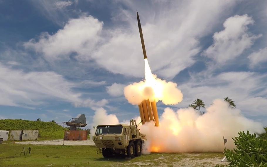A missile defense system launches an interceptor missile from a mobile launcher on a tropical military installation.