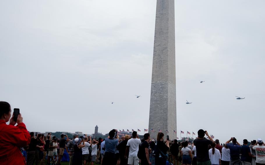 Onlookers watch as helicopters pass by the Washington Monument.
