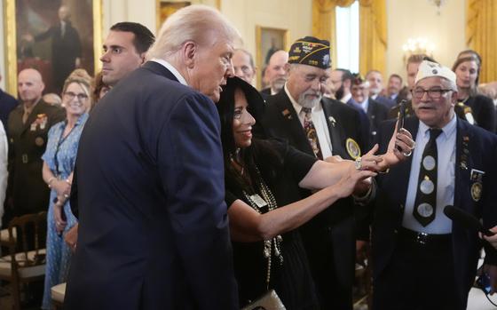 Donald Trump seen from the side leaning forward to be in a person’s selfie.