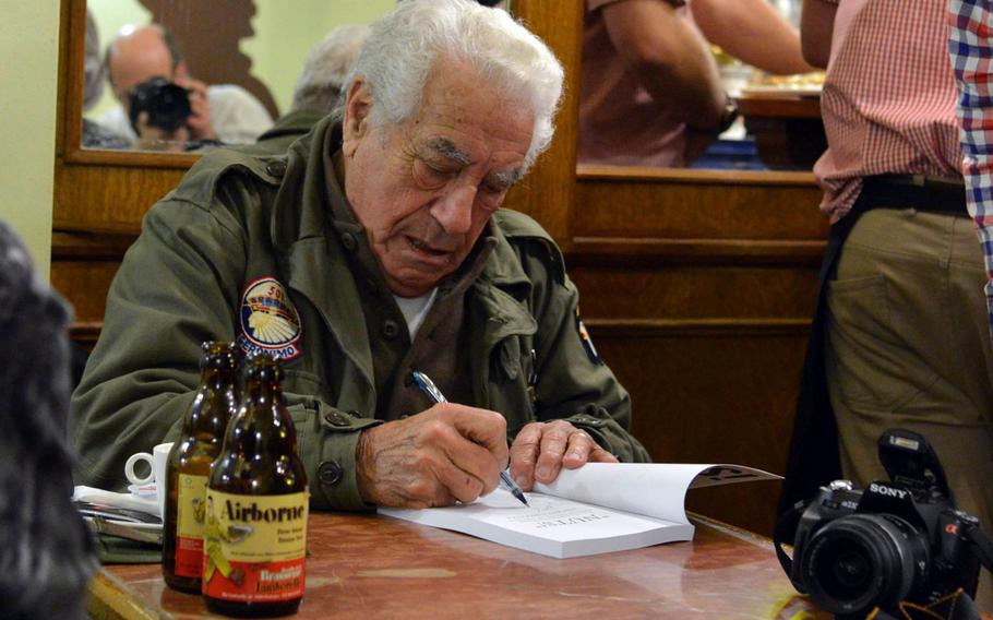 World War II veteran Vincent Speranza autographs a book at Le Nut's Cafe in Bastogne, Belgium, in 2014 during commemorations of the 70th anniversary of the Battle of the Bulge. During the battle, Speranza used his helmet to carry beer to wounded comrades. He died Aug. 2, 2023, at age 98.