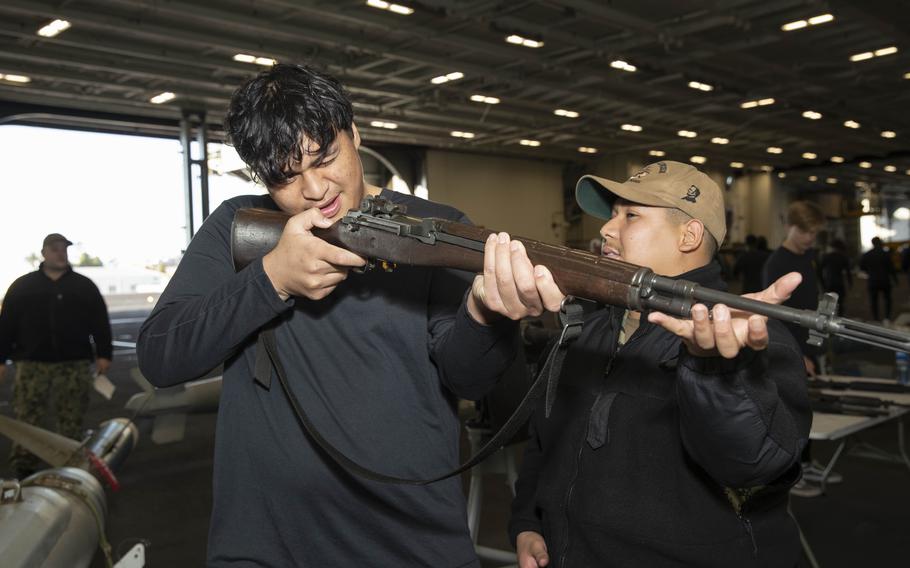 Aviation Ordnanceman Airman Apprentice Jose Andrade, right, from Modesto, Calif., gives a weapons demonstration Dec. 24, 2023, during an open ship tour aboard the Nimitz-class aircraft carrier USS Abraham Lincoln (CVN 72) prior to the 2023 Holiday Bowl. 