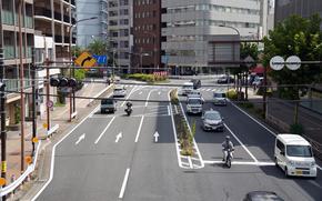 An overhead view of vehicles traveling through a city intersection with buildings in the background.