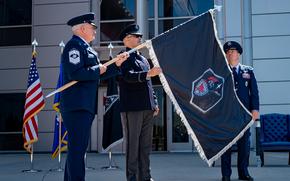 Three men in military dress uniforms unfurl a black flag.