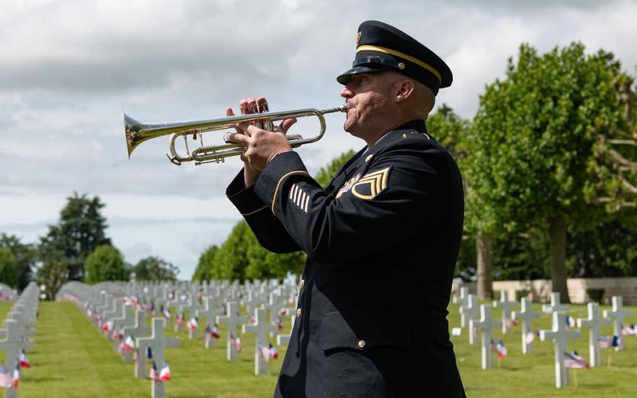A soldier plays a trumpet in the cemetery, with gravestones in the background.