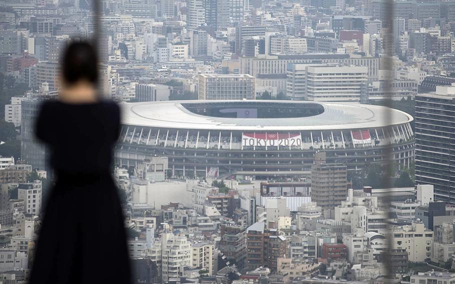 A woman takes photos of the Tokyo skyline, including the Olympic Stadium, from a Shibuya observatory, Tuesday, July 13, 2021. 