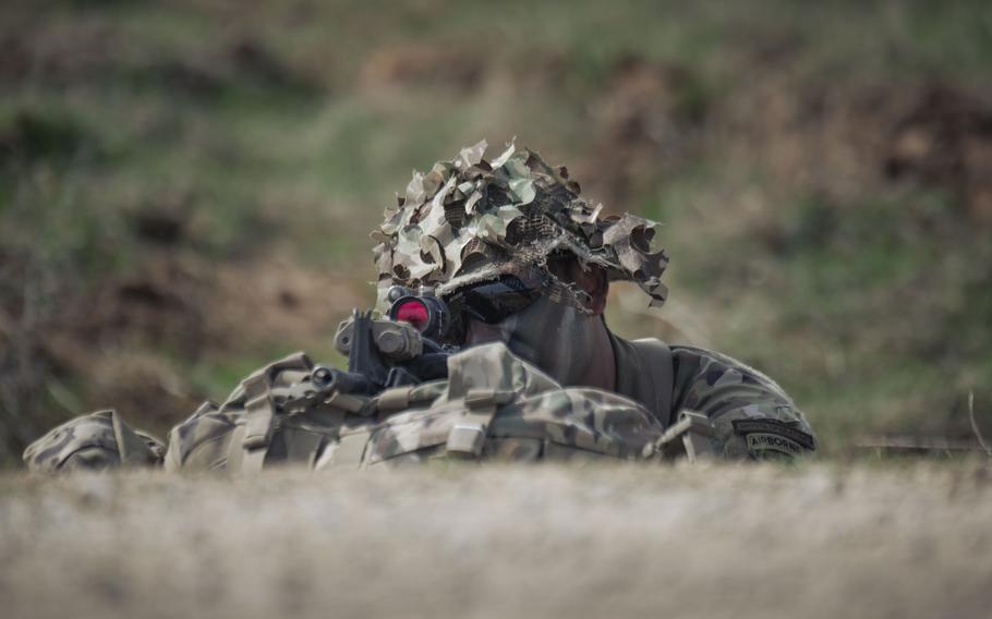 A US Army soldier laying down in the grass with his gun.