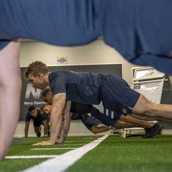 Sailors doing pushups inside a gym.