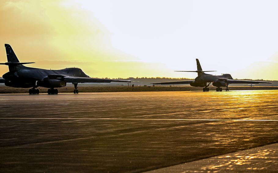 Two military bomber jets taxi on a runway with the setting sun in the background.