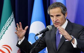 A man in a suit and blue tie gestures with both hands while speaking into a microphone.