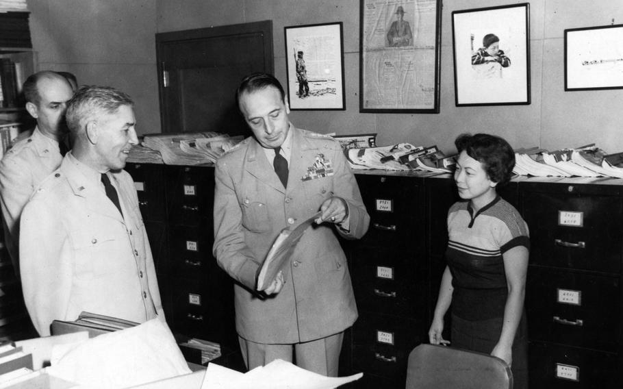 A man looks through some files in a library with people surrounding him