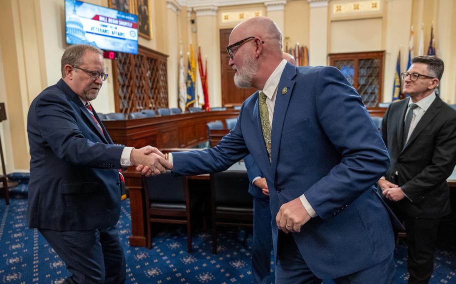 Three men standing together. Two are shaking hands.