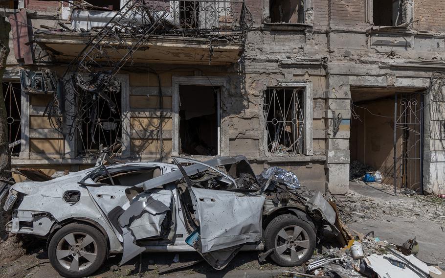 A destroyed car before a damaged building.