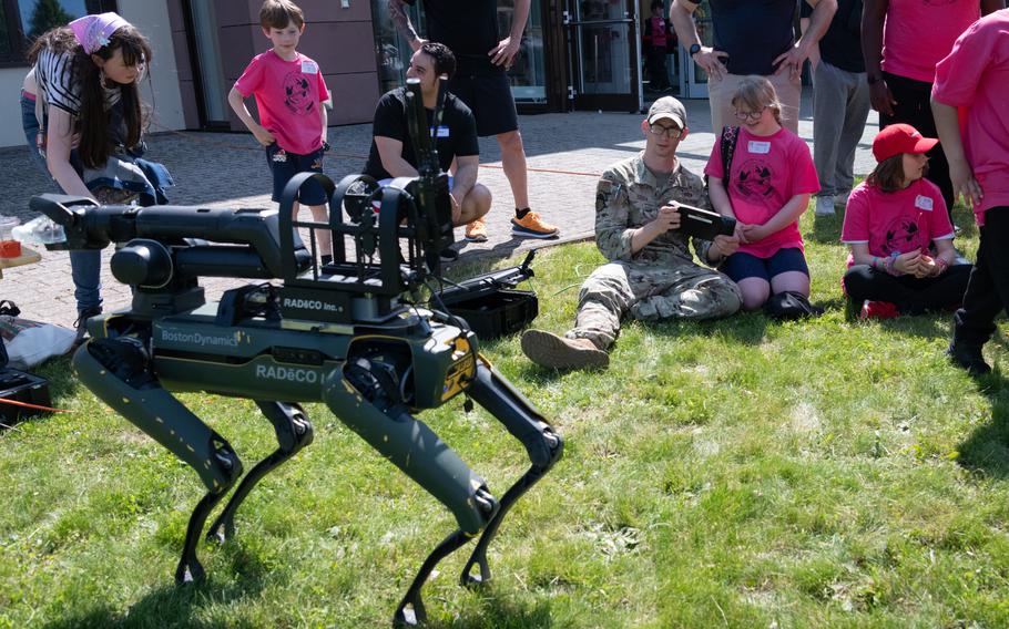 An airman in uniform shows a girl the remote control for a robotic dog. 
