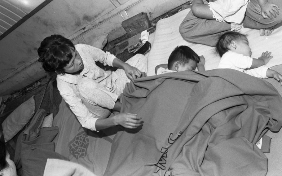 A woman adjusts a blanket placed over infants sleeping on the floor of a plane.