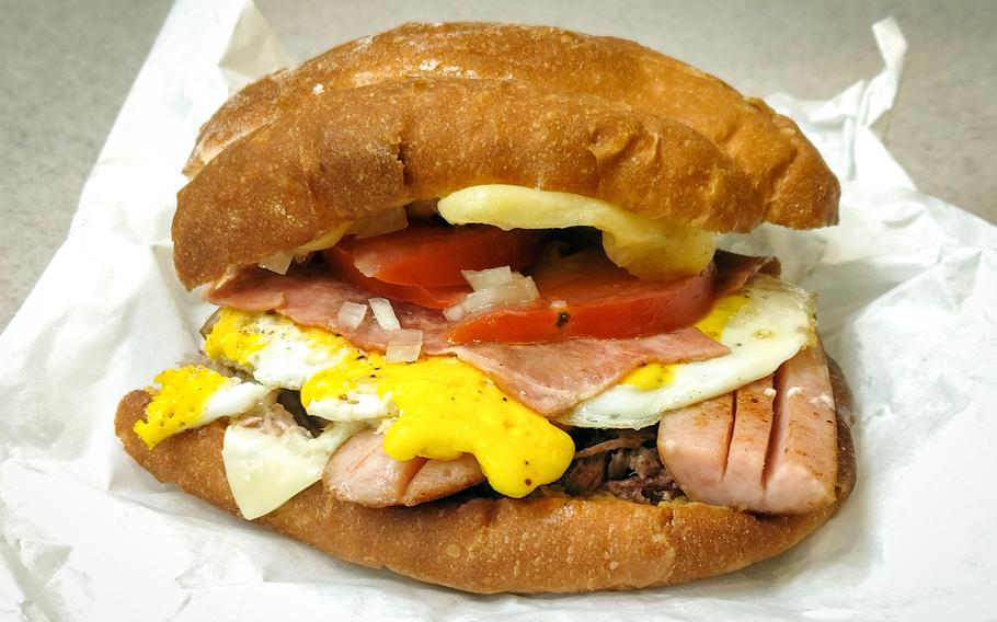 The torta Cubana from Que Rico near Camp Humphreys is filled with pork, sliced cheese, sausage, a sunny-side up egg, sliced bacon, melted cheese, onions, tomato and jalapeño. 