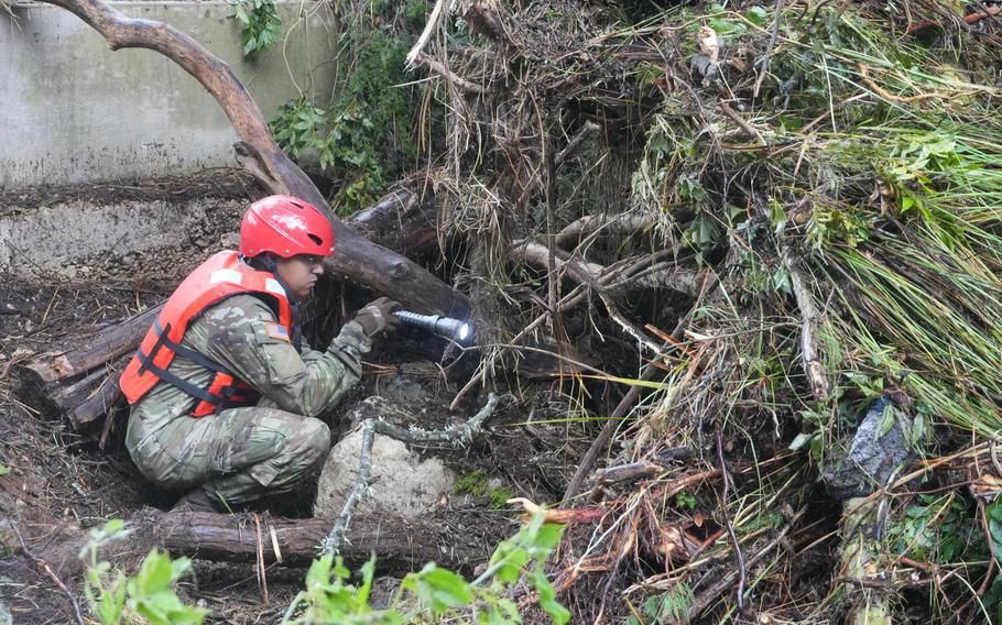 Guard member squats and searches fallen debris using a flashlight.