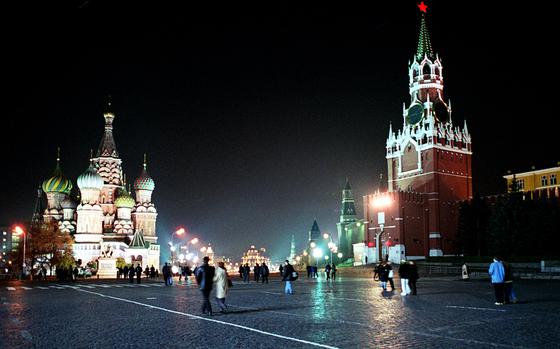 People walk through Red Square in Moscow at night in front of illuminated St. Basil’s Catherdral and the Kremlin.