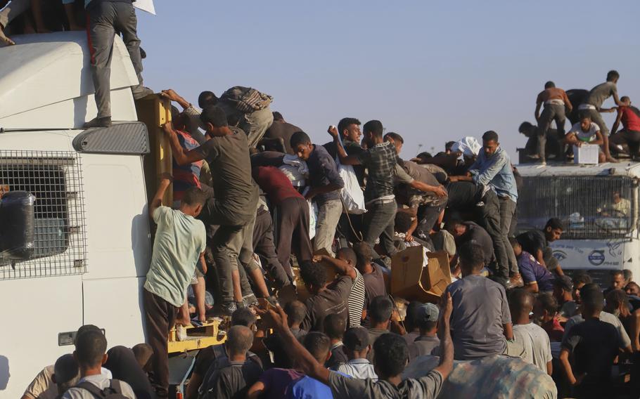 A crowd of Palestinian people climb on the bed of a truck with humanitarian aid.