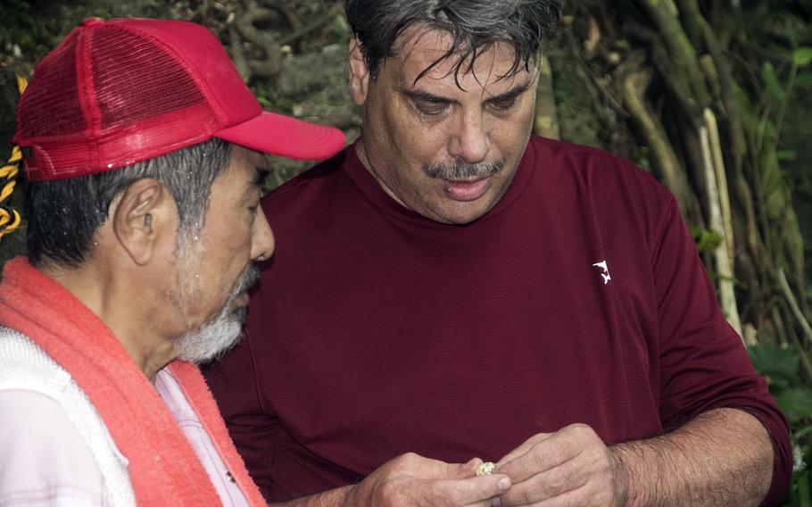 Larry Paleno, right, of Kings Park, N.Y., gazes at a ring that may have belonged to his uncle, Marine Pfc. John Quinn Jr., outside a cave in Itoman, Okinawa, Sept. 10, 2022.