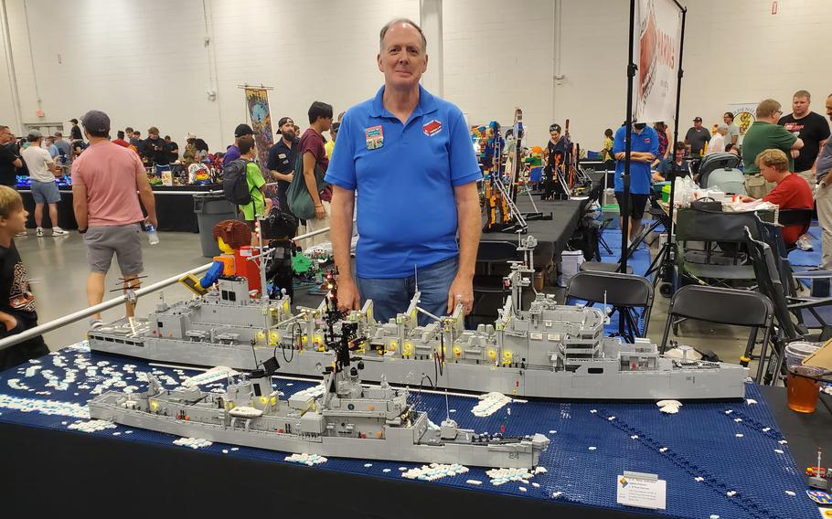 A man stands behind a LEGO model of two Navy ships.