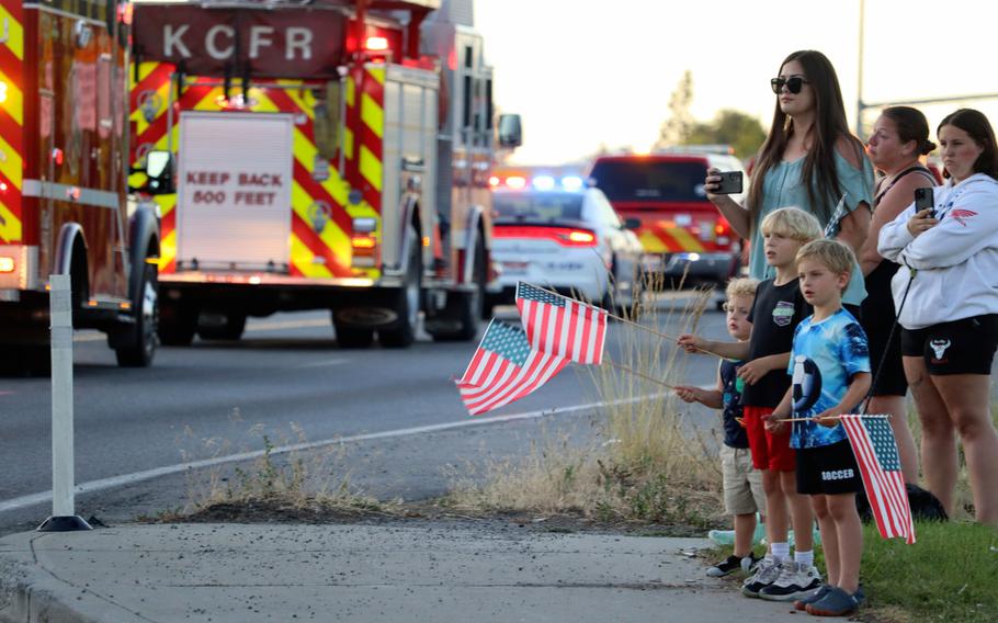 Children wave American flags as a procession of fire trucks and police vehicles drives past.