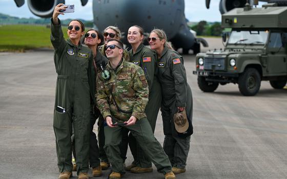 Six Air Force members stand in a group on a runway as one uses a phone to take a selfie photo.