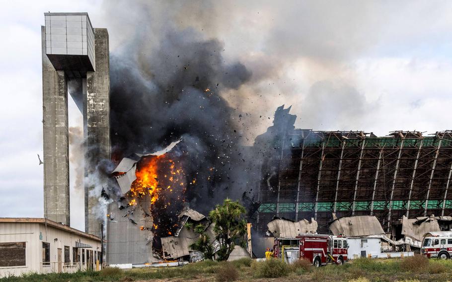 A piece of burning building falls as Orange County firefighters battle a fire affecting the north hangar at the Tustin Air Base in Tustin on Nov. 7, 2023. 