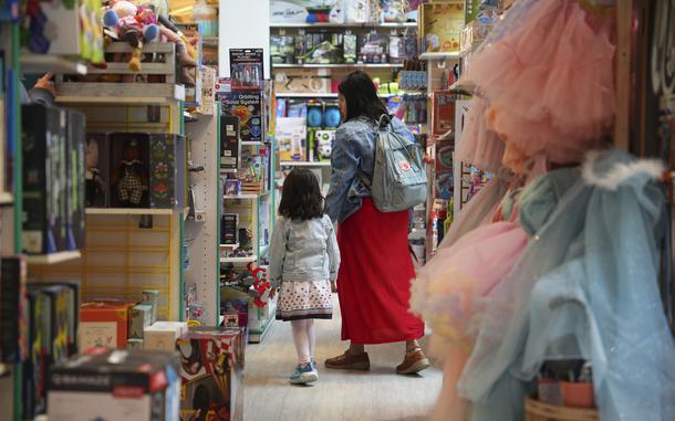 A woman walks with a child through a toy store aisle.
