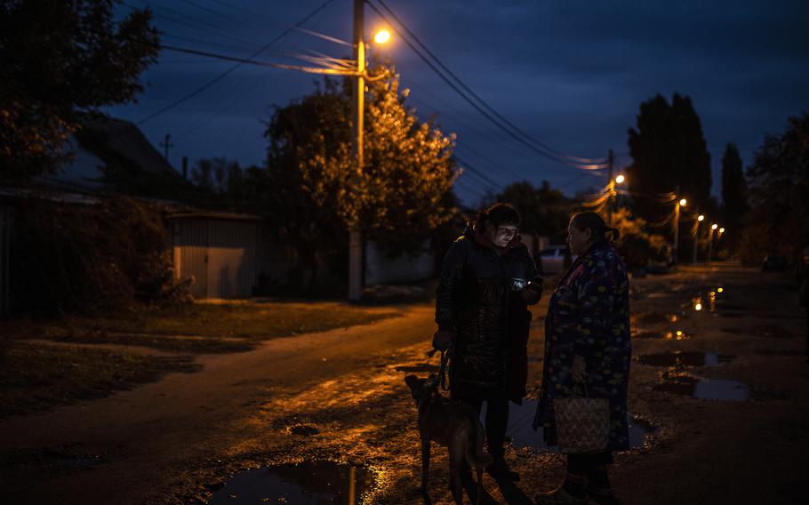 Alyona Harbuz, left, walks her dog before the streetlights go out as she stops to speak to a neighbor, Valentina Fyederova, in Dnipro, Ukraine.