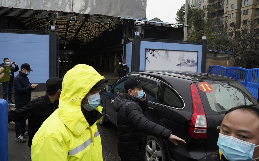 In this file photo dated Sunday, Jan. 31, 2021, security personnel clear the way for a convoy of the World Health Organization team to enter the Huanan Seafood Market on the third day of field visit in Wuhan in central China's Hubei province. International scientists have examined previously unavailable genetic data from samples collected at a market in China close to where the first human cases of COVID-19 were detected and said they have found suggestions the pandemic originated from animals, not a lab.