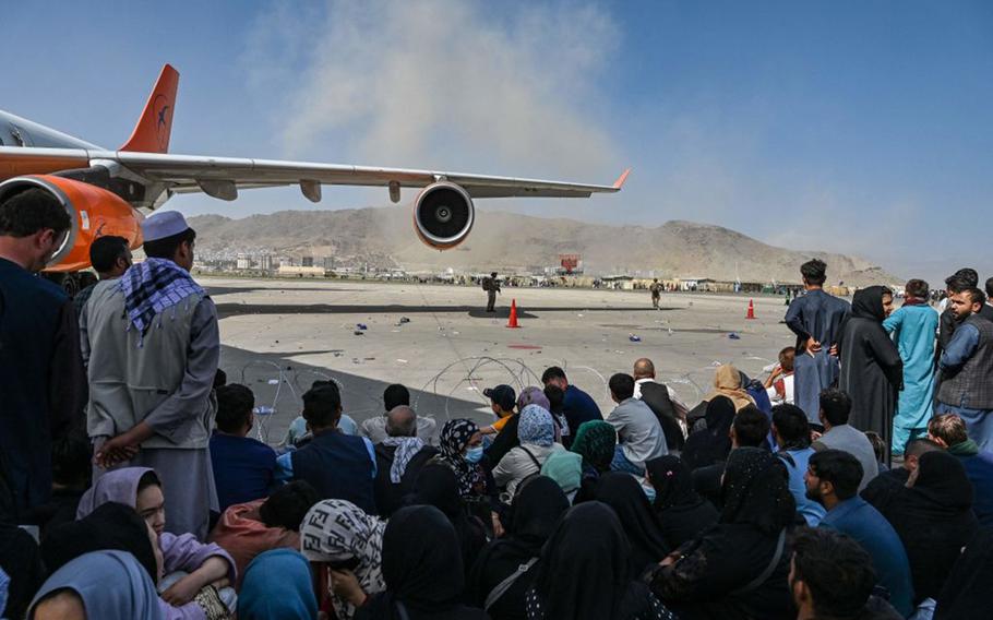 Afghan people sit as they wait to leave the Kabul airport in Kabul, Afghanistan, on Aug. 16, 2021, as thousands of people mobbed the city’s airport trying to flee the Taliban.