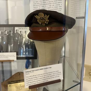 A WWII-era military cap is seen on a mannekin head behind a glass encasing.