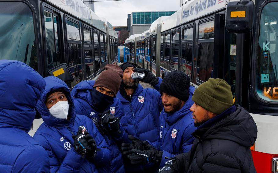 A migrant drinks canned water near Chicago Transit Authority buses at the city’s migrant “landing zone” on Jan. 10, 2024, while Angelo Traviezo, second from right, of Venezuela, talks with other migrants. At least eight CTA buses are being used at the site as temporary shelters for recently arrived migrants.