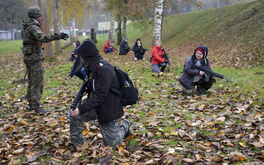 Polish civilians kneel as they listen to a soldier at the Military University of Technology in Warsaw, Poland, explain how to survey their surroundings while marching through dangerous areas, as part of a familiarization course Nov. 5, 2022.