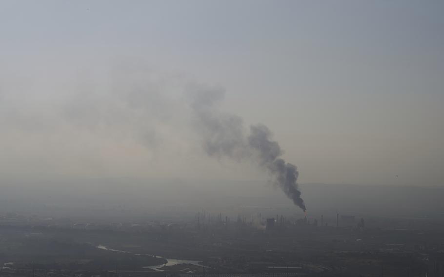 A hazy view of an oil refinery in the distance, with smoke billowing out.