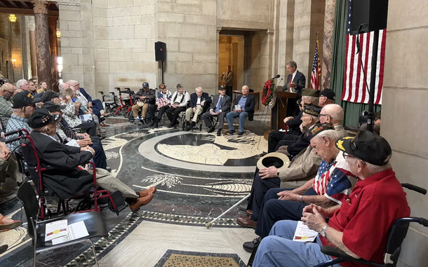 Veterans seated in a circle while a man in a suit speaks at a podium.
