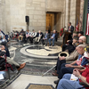 Veterans seated in a circle while a man in a suit speaks at a podium.
