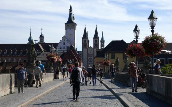 With the town hall tower and church steeples in the background, people walk across Wuerzburg, Germany’s Alte Mainbruecke, the old stone bridge across the Main River, into the old town.
