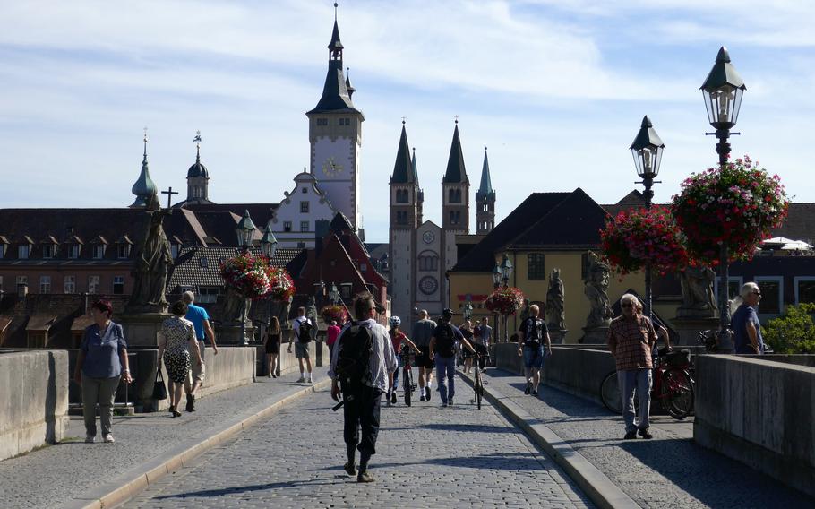 With the town hall tower and church steeples in the background, people walk across Wuerzburg, Germany’s Alte Mainbruecke, the old stone bridge across the Main River, into the old town.