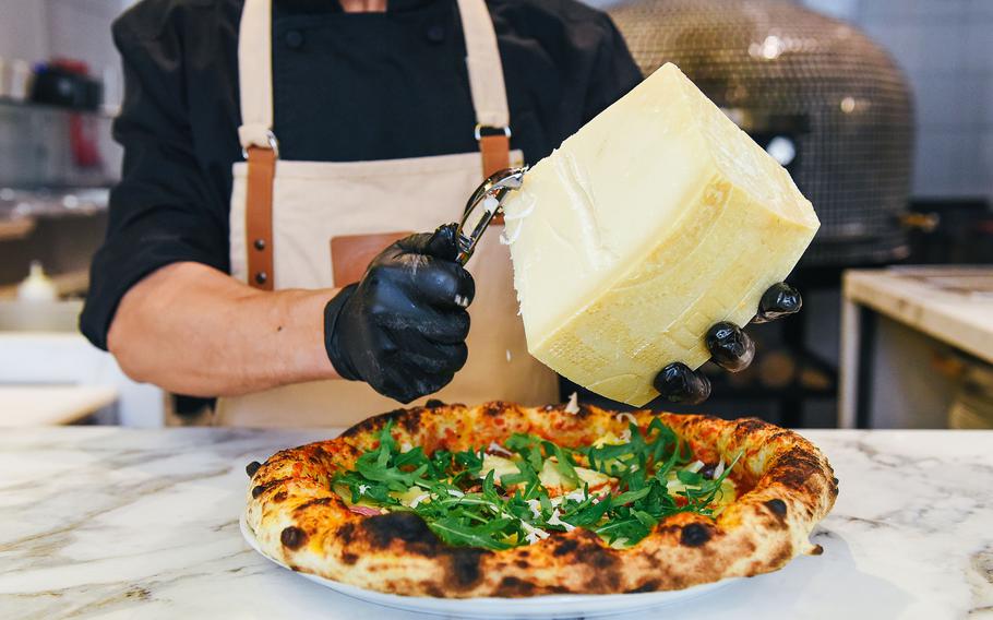 A cook grates Parmasan cheese on a pizza.