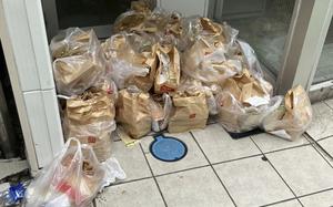 A large pile of McDonald’s takeout bags and plastic bags stacked on a tiled floor outside glass doors. The brown paper bags with McDonald’s logos are bundled together in clear plastic bags.