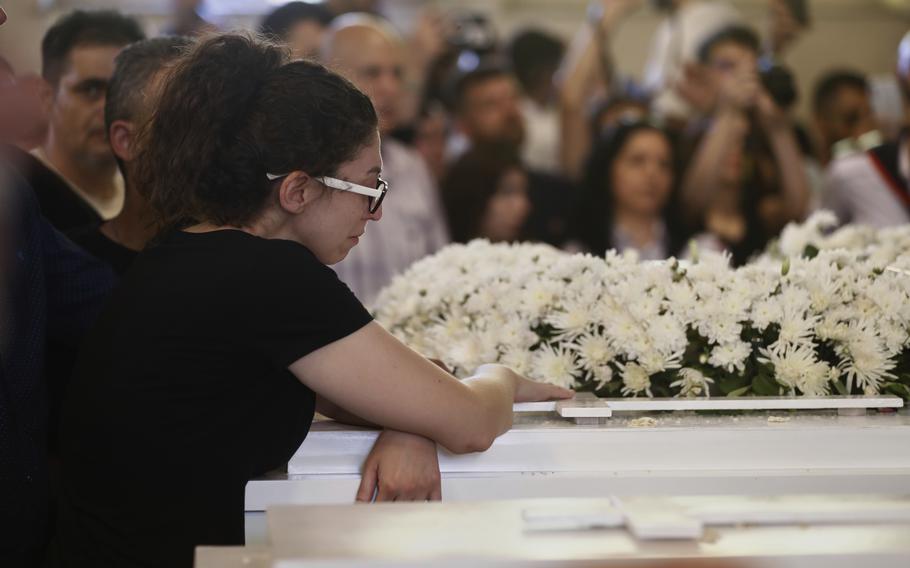 A woman in a black shirt folds her arms next to a coffin.