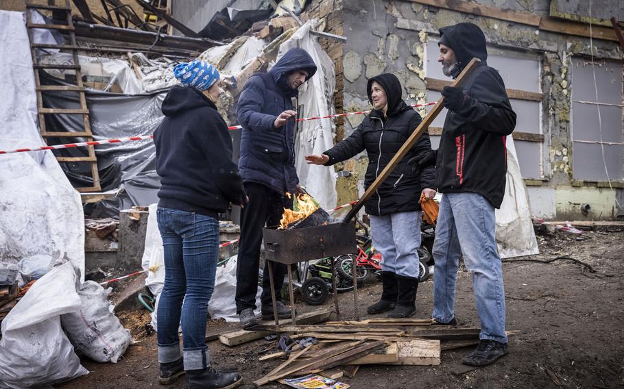 Serhiy Kaharlytskiy, 42, center left, whose wife was killed when a Russian missile landed near their house in Kyiv on New Year’s Eve, and his wife’s friend, Daria Khizhchuk, center right, warm their hands as volunteers clear rubble.