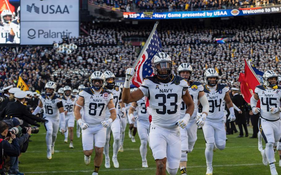 A Navy player carrying an American flag leads his team onto the field.