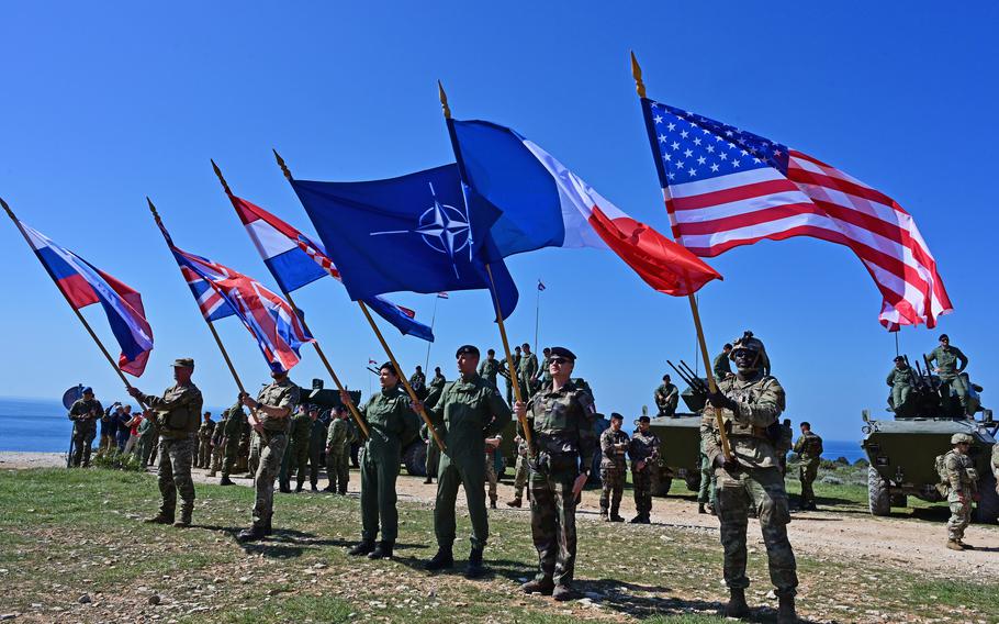 Soldiers carrying their flags of their respective countries and the NATO flag in the middle.