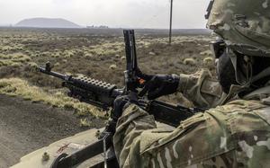 A U.S. soldier in uniform loads a mounted machine gun in dry, open terrain.