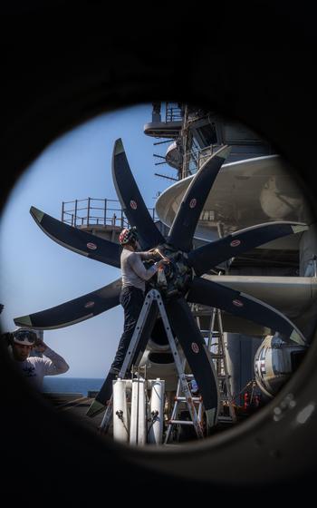 A sailor performs maintenance on the turbine of an aircraft.