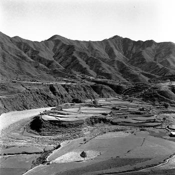 Plots of land are seen in a mountainous valley from above.